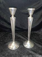 Pair of tall polished sterling silver weighted candle holders standing upright on a black fabric background.