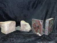 Two sets of stone bookends, one set rough natural stones and the other set polished maroon-green stones on metal slats, against a black background.