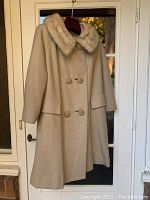 Full view of vintage beige double-breasted coat with fur collar hanging on door.