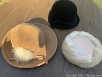 Three vintage ladies hats: camel felt with feather, black cloche velour, and beige pillbox with white fur trim.