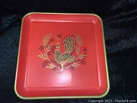 Full view of square red tray with gold-edged border and peacock design in the center