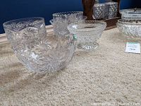 Wide view of several crystal bowls and serving platters showing detailed cut patterns and shapes on beige carpet.