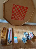 Overview of the lot showing wooden and cardboard cribbage boards, pile of playing card decks, and octagonal wooden checkers/chess board.