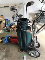 Golf clubs and golf bag mounted on metal golf push cart with wheels in garage setting, showing entire set and condition.