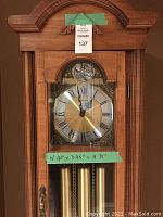 Front view showing clock face with Tempus Fugit and Westminster chime, glass door closed, reveals weights and pendulum, taped with lot number and dimensions.