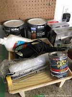 Overview photo showing paint tray, rollers, weatherproofing cans, Flex Seal can, paint primer bottle, door handles, and Black & Decker paint remover cord.