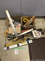 Overview of hand tools including saws, carpenter's square, and levels in two cardboard boxes.