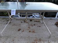 Photo of rectangular glass-top patio table showing table surface and metal frame with signs of wear and some rust on the legs.