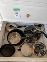 Drawer with assorted pots and pans including small frying pans, saucepans, and pots with lids.