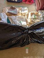 Large foam mattress topper wrapped in black plastic, laid on floor with various folded bedding sets nearby.
