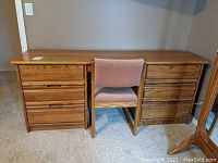 Front view of large solid wood desk with two drawer cabinets and matching chair with pink fabric upholstery.