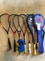 Photo showing six rackets lying on the floor with two racket covers and a pair of blue wristbands arranged in front of them.