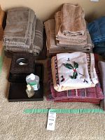 Stacks of beige, gray, blue, and decorative towels with brown tissue box cover and trays on carpet.