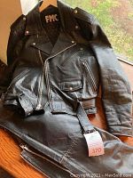 Photo of the black leather jacket and pants on wooden surface showing overall condition and style