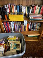 Bookshelves filled with various books including religious, fiction and other topics with a plastic bin full of more books in front.