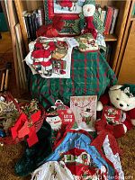 Photo showing Christmas fabric items including aprons, and decorative signs with Santa, along with plush figures and ornaments arranged on a green and red fabric.