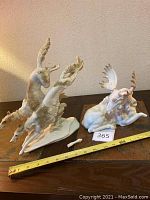 Photo showing the two ceramic figurines: the running Salukis and reclining moose, alongside measuring tape and broken pieces visible