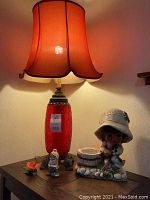 Vintage red glass lamp with fabric shade illuminated, displayed on console table with tile insets, with small figurines arranged nearby.
