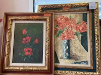 View of two framed floral paintings side by side, smaller painting has red roses and dark green background, larger painting with peach chrysanthemums and cream fabric background.