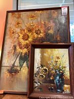 Two framed floral still life paintings stacked, larger with sunflowers, smaller with blue vase and sunflowers.