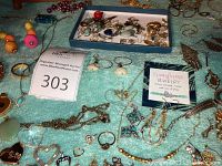 Top view of towel covered surface with assorted jewelry including heart-shaped pendants, chain necklaces, bracelets, rings, charms, and a display tray at top.