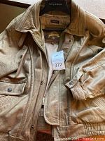 Tan leather or suede jacket close-up showing collar, snap buttons, and pocket details.