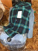 Blue-green plaid button-up sweater laid out on top of folded jeans/slacks, showing buttons and pattern detail