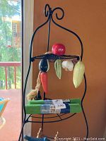 Black metal corner wire shelf with ceramic vegetables on top and hanging, a green shelf liner folded on the shelf