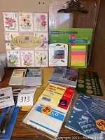 Photo of alphabet greeting cards, clipboard, flash drive package, sticky notes, name badge labels, oil pastels, and assorted labels