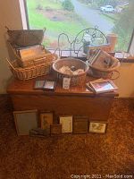 Storage chest, baskets filled with books and seashells, assorted picture frames, and a metal hanging decoration on table and floor