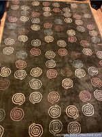 Photo of one of the two area rugs with olive green background and multicolor spiral designs.
