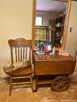 View of wooden chair holding glass jars and tray alongside tea cart and mirror with various decorative items placed on tea cart surface.