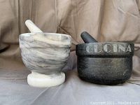Front view of white marble and grey stone mortar and pestle sets, showing 'CUCINA' engraving on grey mortar.