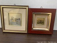 Two square framed pictures side by side on a shelf, one with a helicopter design in silver tone.