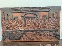 Full view of the carved wooden plaque showing The Last Supper scene with Jesus and disciples seated at a long table in a room with detailed background.