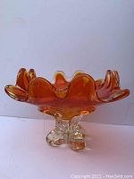 Side view of an orange glass vase with ruffled edges and clear glass footed base.