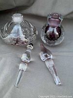 Clear and purple controlled bubble glass perfume bottles with their respective stoppers, showing overall appearance and size.