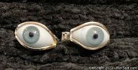 Pair of eyeball cufflinks displayed side by side on a black fabric surface.