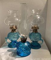 Pair of blue glass finger lanterns with clear chimneys on white cloth background
