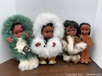 Photo shows all four dolls but two main dolls are the focus: one in green/white fur parka and one in brown leather clothing with cape.
