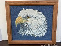 Framed artwork showing a side profile of a bald eagle head painted in oil on denim fabric with a wood frame.