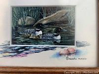 Close-up of artwork showing two loons, rocks, reeds, and signature by Madu Masco.