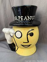 Front view showing smiling Mr. Peanut face on yellow ceramic cookie jar with black top hat marked Mr. Peanut and white gloved hand handle