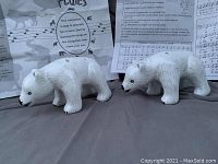 Photo showing two white pottery polar bear flutes positioned side by side with sheet music and instructions in the background.