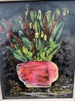 Framed tile art piece showing a vibrant plant in a pink pot with raised protruding textures that appear to be stone or glass, signed by the artist.