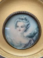 Close-up photo of the lady portrait print under convex glass in an oval yellow velvet frame, showing detailed face and upper torso of the lady in period dress.