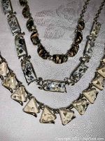 Photo showing three vintage Coro Lucite necklaces: triangular cream flecked, rectangular marbled, black and gold swirled pieces, all on silver-tone metal chains.