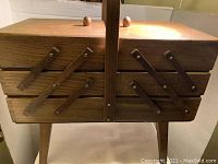 Wooden accordion-style sewing box with central handle. Side compartments with metal hinges allowing folding.