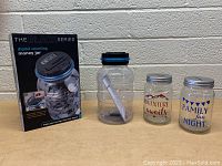 Photo showing The Black Series digital counting money jar with box, and two glass money jars with printed text designs.