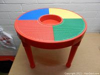 Front and top view of the round children's table with Lego-style building surface divided into color segments red, blue, yellow, green with red legs